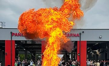 Ogromny płomień ogna. W tle budynek straży oraz przyglądający się ludzie.